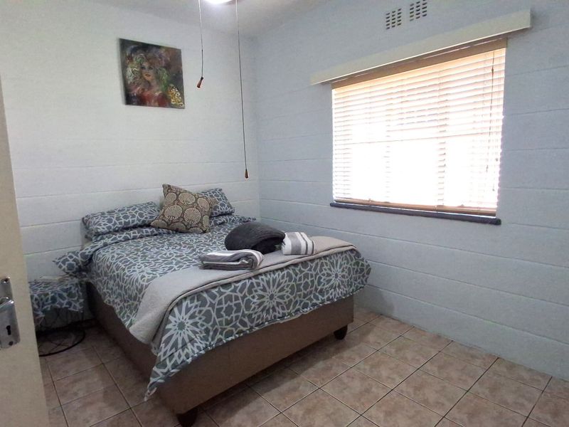 A functional bedroom featuring tiled flooring, a window with venetian blinds, and a ceiling light fixture.