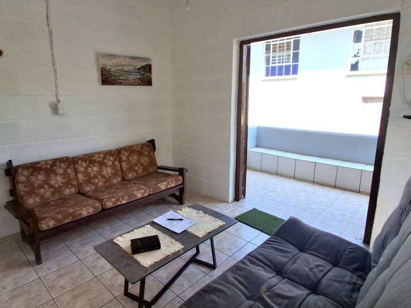 A living room featuring tiled flooring and exposed blockwork walls, with direct access to an outdoor patio area.