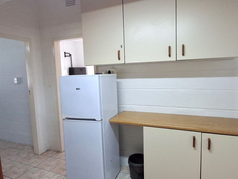 A functional kitchen area featuring laminate countertops, built-in cabinetry, and tiled flooring, offering a dated aesthetic ready for modernization.