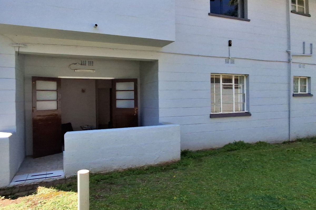 Ground floor apartment exterior featuring a small patio area with double door access and surrounding lawn space.