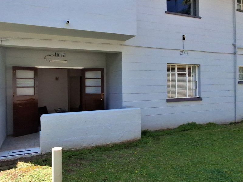 Ground floor apartment exterior featuring a small patio area with double door access and surrounding lawn space.