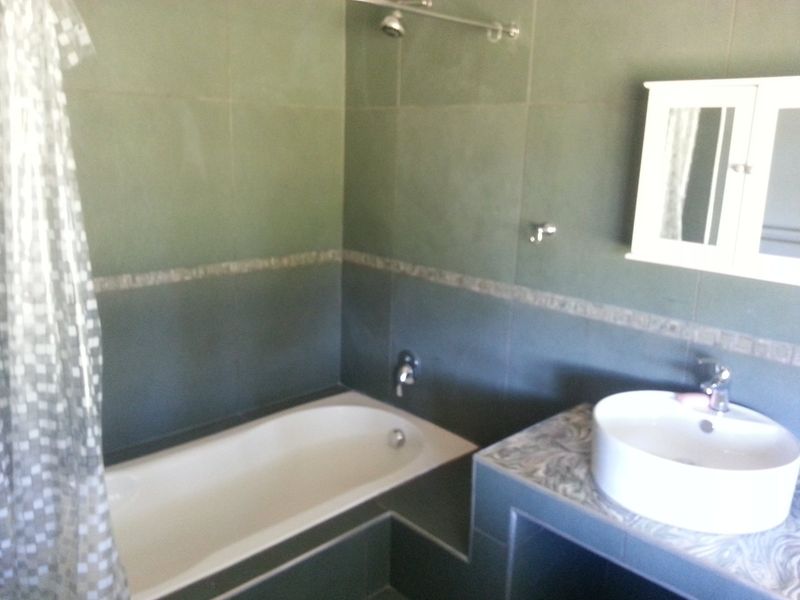 A bathroom featuring dark green wall tiles, a built-in bathtub with shower, and a vessel sink set on a tiled vanity.