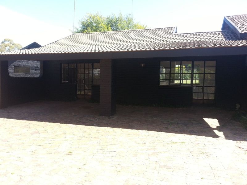 A front exterior view of the house featuring a covered entrance, brick paving, and dark-painted brick walls with steel-framed windows.