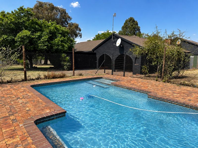 Outdoor pool area featuring a swimming pool with brick paving surround and a view of the rear building elevation.