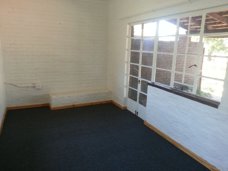An empty living area featuring painted brick walls, dark carpeting, and large multi-pane windows providing natural light and access to the exterior.