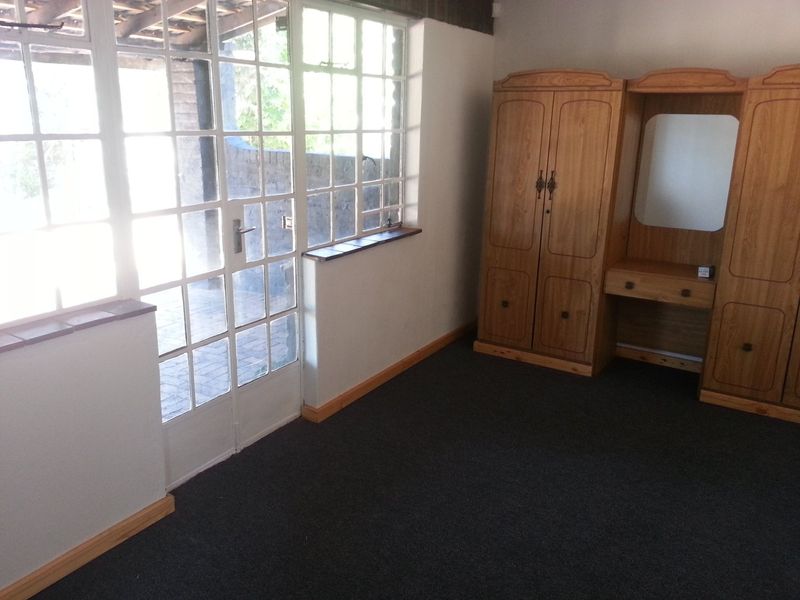 A bedroom featuring timber-framed glass doors leading to an outdoor area, carpeted flooring, and neutral walls.