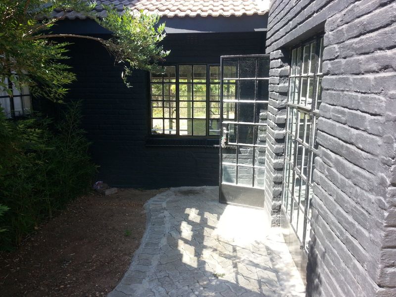 A rear exterior view featuring dark painted brick walls, steel-framed windows and doors, and a paved walkway leading to the entrance.