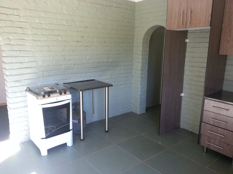 A kitchen area featuring exposed brick walls, tiled flooring, an arched doorway, and basic cabinetry with a freestanding gas stove.