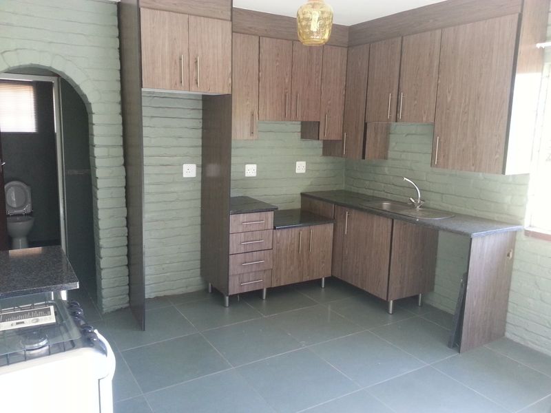A functional kitchen featuring wood-look cabinetry, granite-style countertops, and tiled flooring, set against a unique painted brick wall with an arched entry.