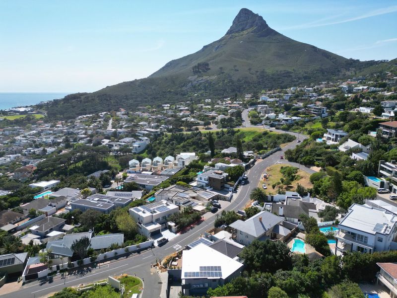 An aerial view of a residential neighbourhood featuring homes with solar panels and swimming pools, set against a mountain backdrop.