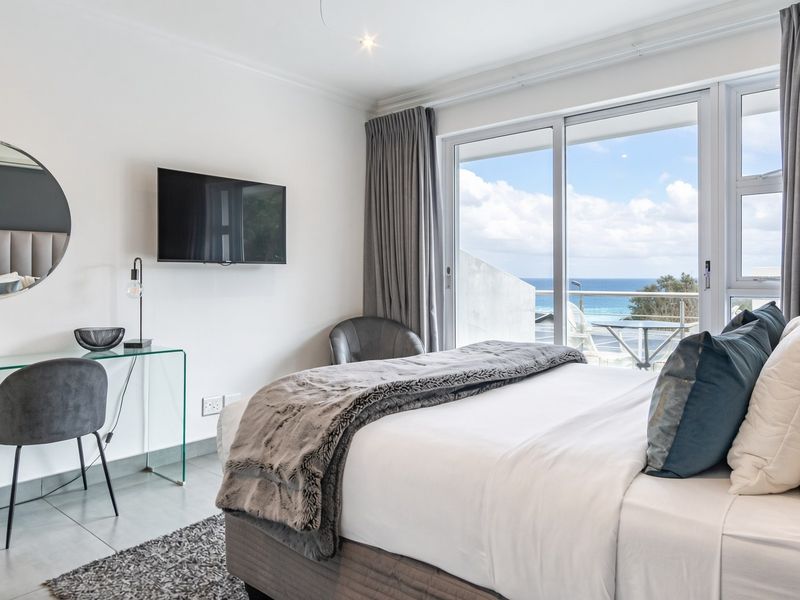 Modern bedroom featuring tiled floors, recessed lighting, and a large sliding glass door providing access to a balcony with ocean views.