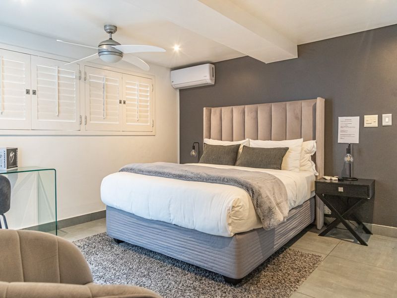 A well-maintained bedroom featuring tiled flooring, plantation shutters, a ceiling fan, and a wall-mounted split-system air conditioner.