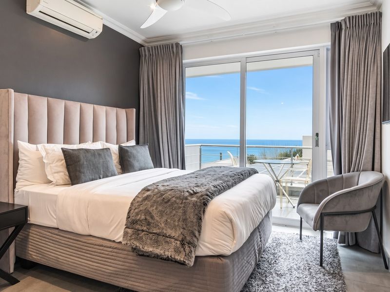 A well-maintained bedroom featuring a split-system air conditioner, ceiling fan, and sliding glass doors that open onto a balcony with ocean views.