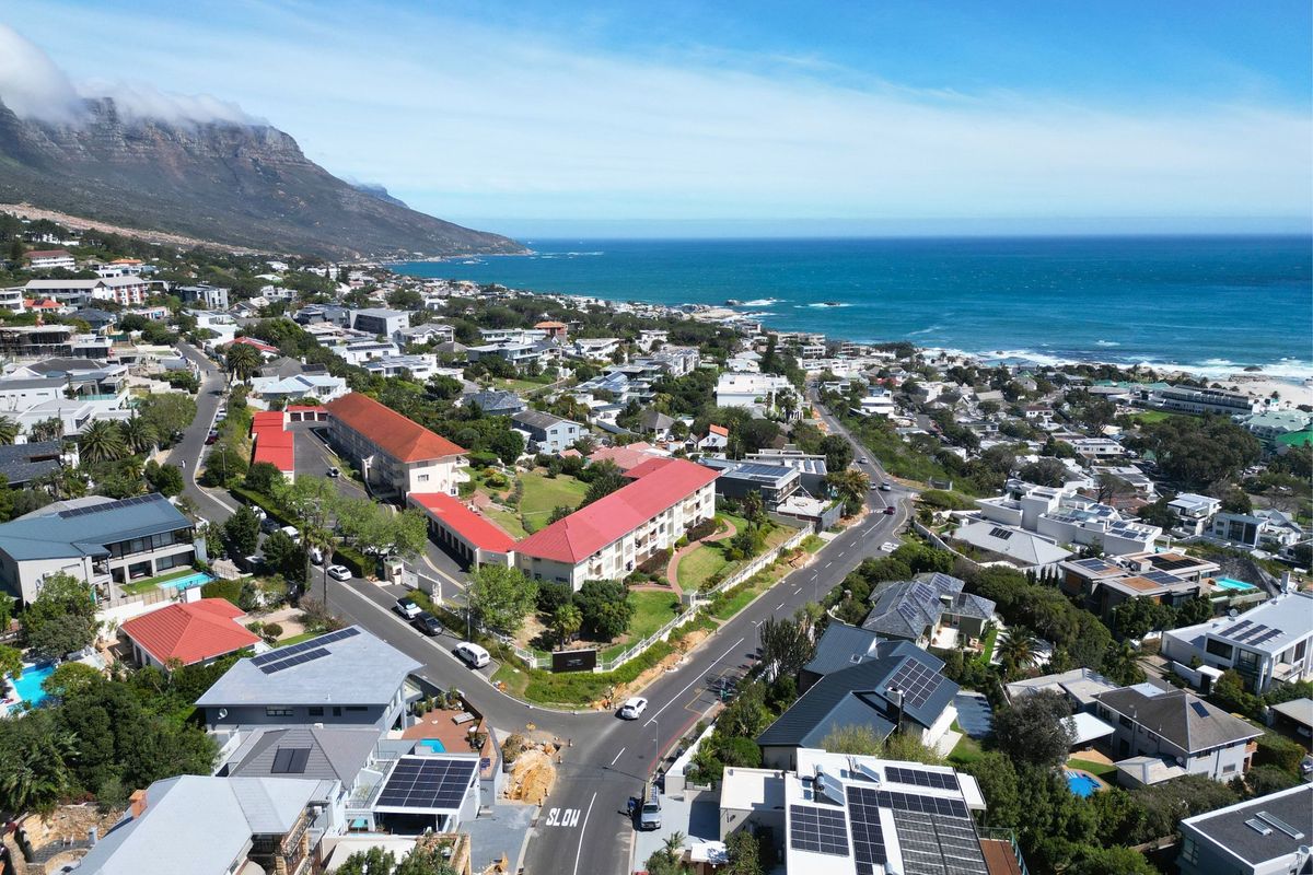 An aerial view of a coastal residential neighborhood featuring multiple properties with solar panels, red tiled roofs, and proximity to the ocean.