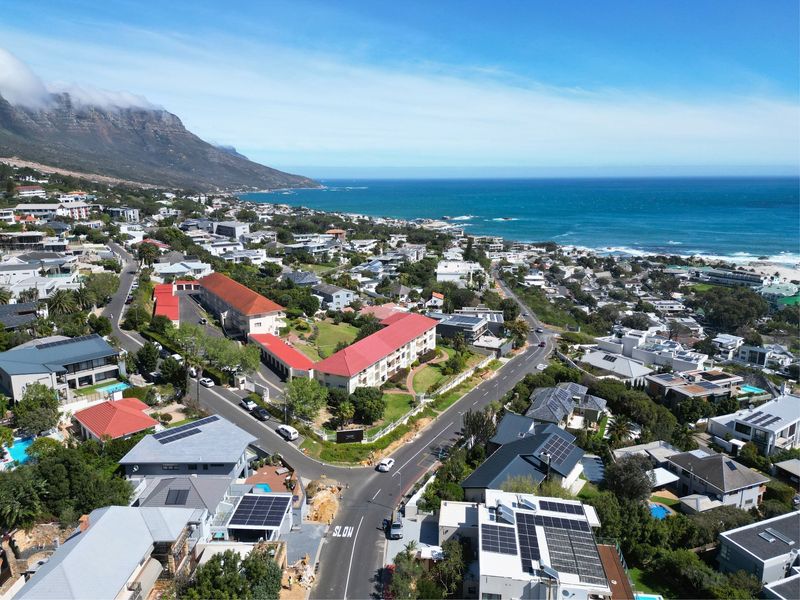 An aerial view of a coastal residential neighborhood featuring multiple properties with solar panels, red tiled roofs, and proximity to the ocean.