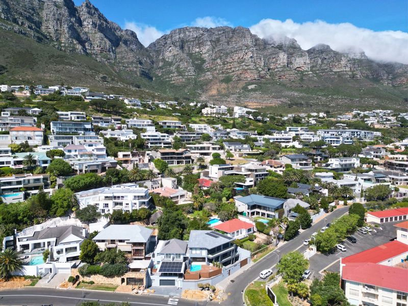 An aerial view of a residential neighborhood nestled against a mountain range, showcasing various homes with pools and solar installations.