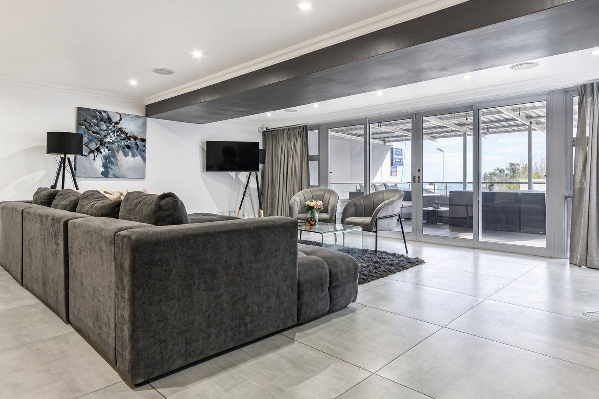 Spacious living room featuring large format floor tiles, recessed downlighting, and expansive sliding glass doors providing seamless access to the outdoor patio area.