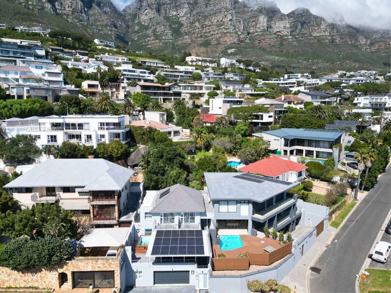 Aerial view of a residential property featuring solar panels, a swimming pool, and a deck, situated in a hillside neighborhood.