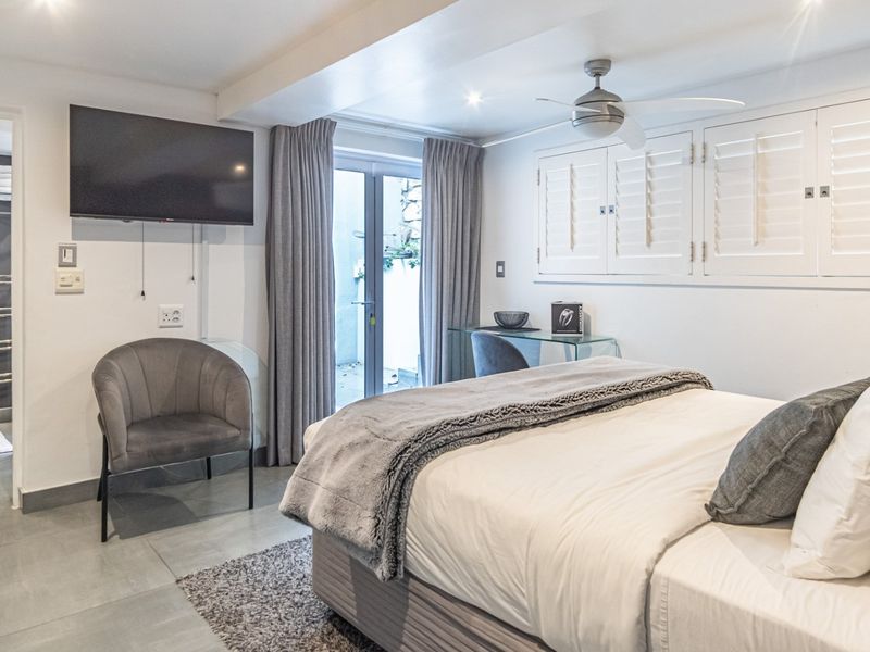 A well-maintained bedroom featuring tiled flooring, a ceiling fan, plantation shutters, and direct access to an outdoor area through glass sliding doors.