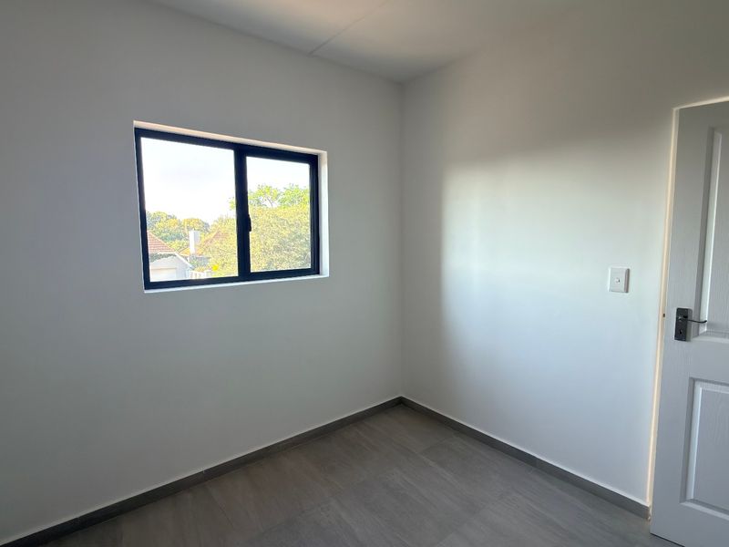 A clean, empty bedroom featuring modern laminate flooring, neutral white walls, and a black aluminium window frame.