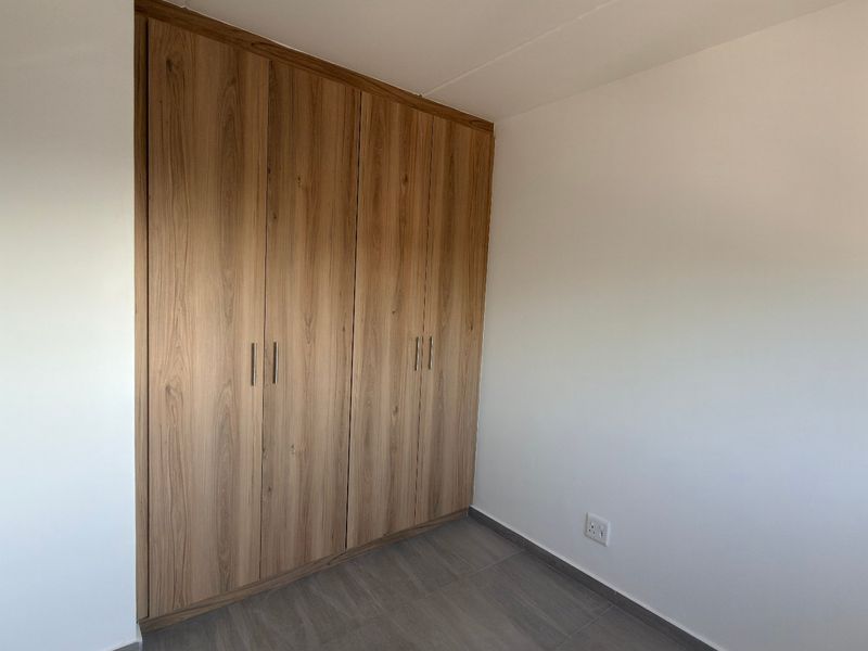 A clean, empty bedroom featuring modern wood-finish built-in cupboards and neutral tiled flooring, providing a versatile space ready for personalization.