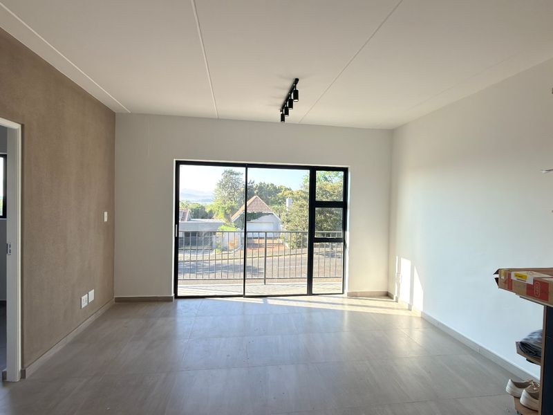 Bright open-plan living area featuring modern tiled floors, track lighting, and a large sliding door leading to an outdoor balcony.