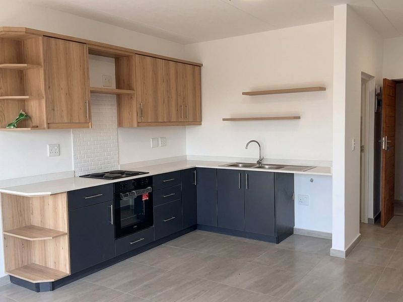 Modern kitchen featuring two-tone cabinetry, built-in oven and hob, subway tile backsplash, and neutral tiled flooring in an open-plan layout.