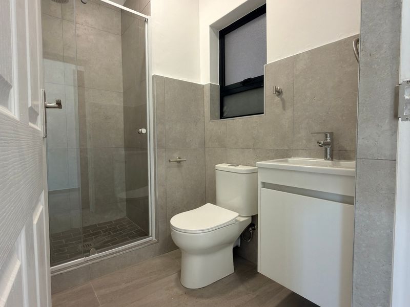 Modern bathroom featuring a glass-enclosed shower, wall-mounted vanity with mixer tap, and neutral grey floor-to-ceiling tiling.
