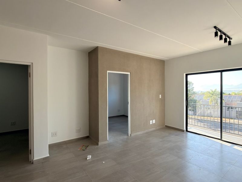 A bright, empty living area featuring modern tiled floors, an accent wall, and a sliding glass door leading to a balcony with scenic views.