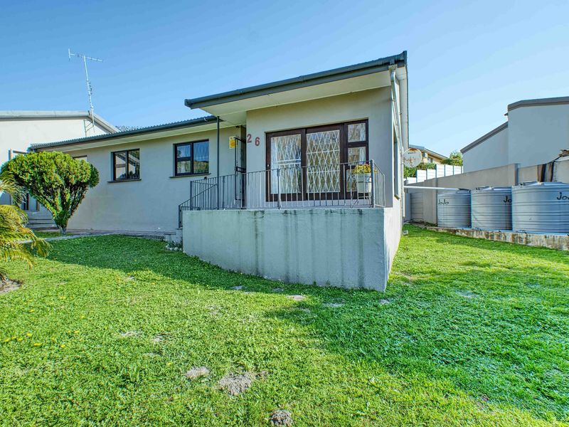 Rear view of the property featuring a raised patio, security gate, and multiple water storage tanks set within a grassed garden area.