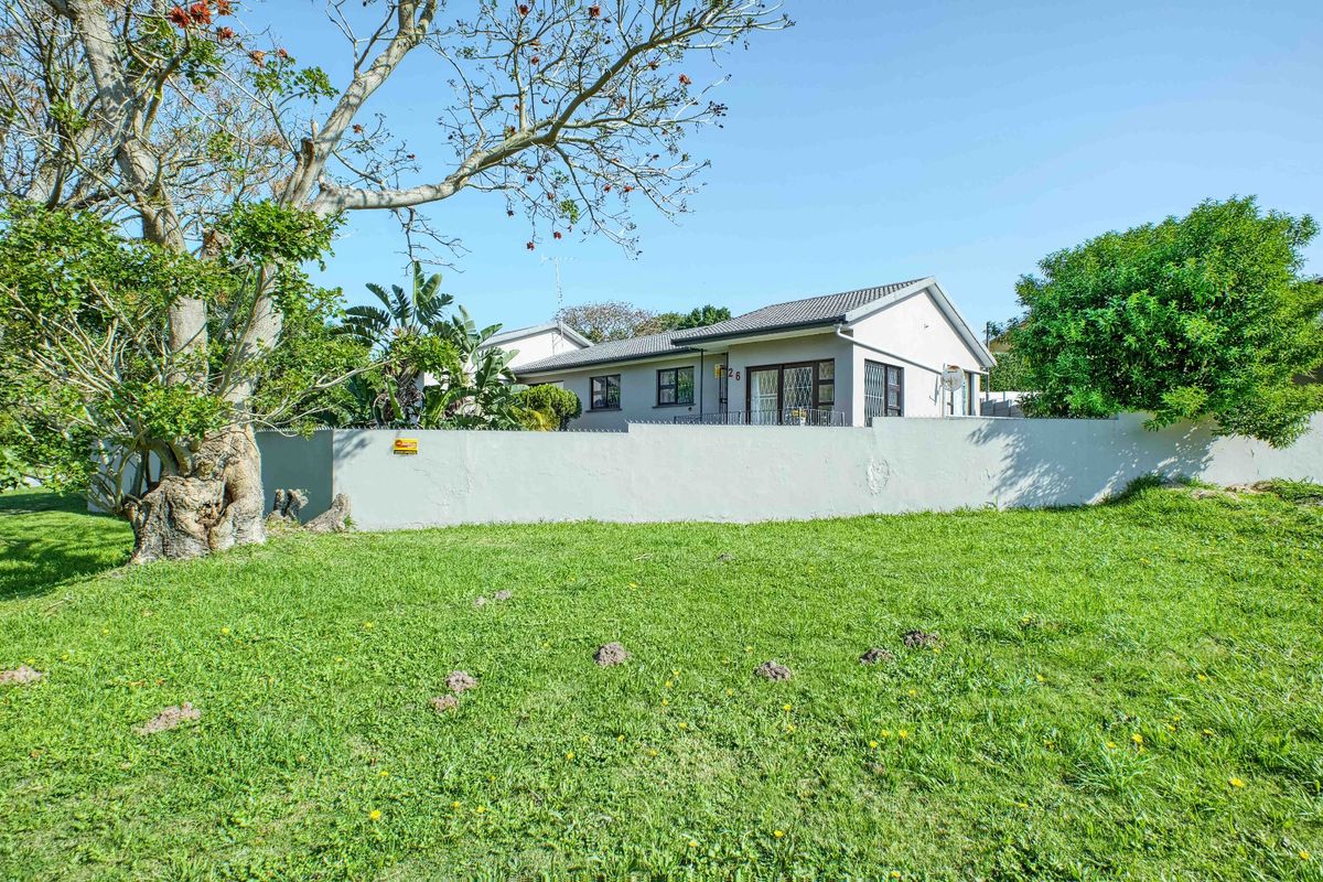 A view of the rear exterior of the house featuring a large lawn, perimeter wall with security spikes, and a tiled roof.