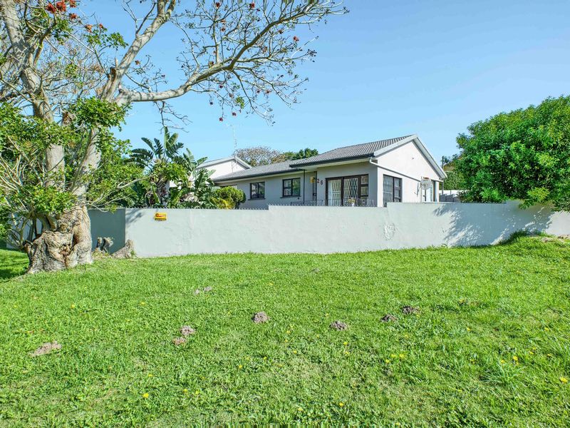 A view of the rear exterior of the house featuring a large lawn, perimeter wall with security spikes, and a tiled roof.