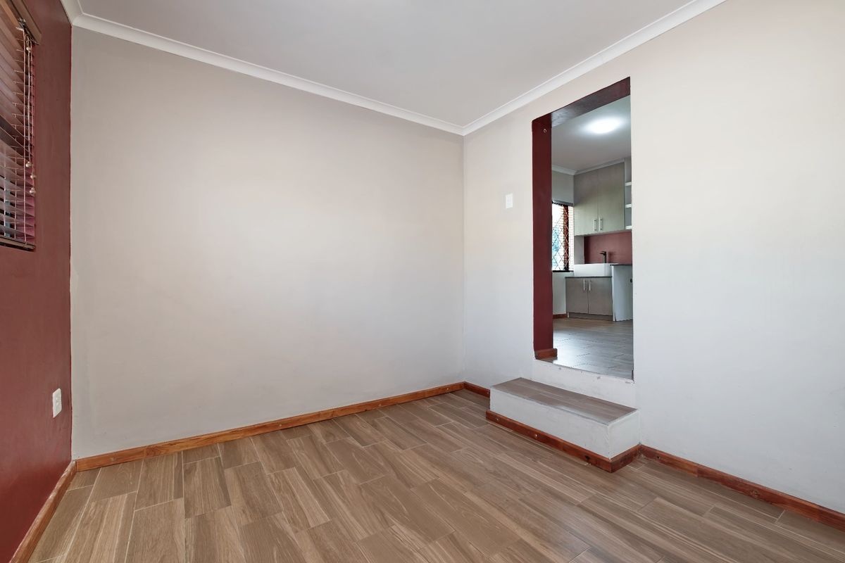 An empty living area featuring timber-look floor tiles and a raised step leading into the adjacent kitchen space.