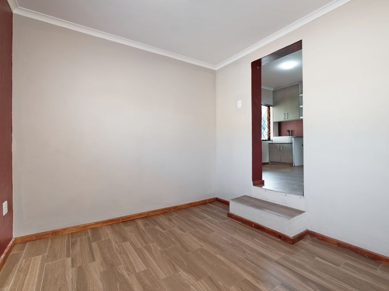 An empty living area featuring timber-look floor tiles and a raised step leading into the adjacent kitchen space.