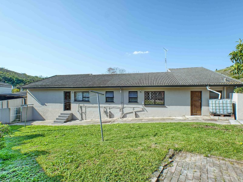 Rear view of the house featuring a tiled roof, concrete patio area, and a spacious lawn with paved sections.