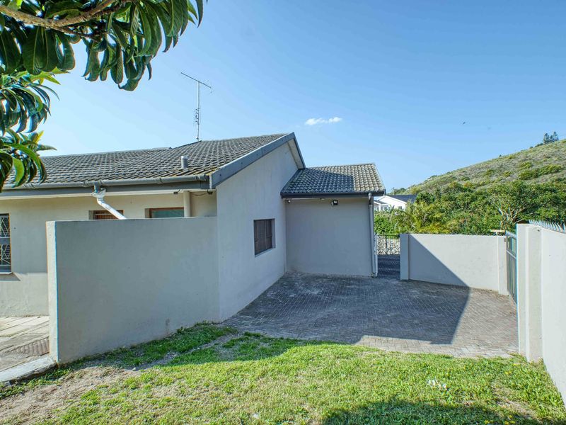 Rear exterior view of the property featuring a paved driveway, boundary walls with security spikes, and a tiled roof structure.
