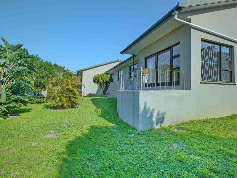 Rear view of the property featuring a concrete patio area, metal security window bars, and a surrounding garden space.
