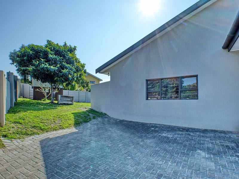 A view of the rear exterior area featuring a paved driveway, boundary wall, and a well-maintained garden space.