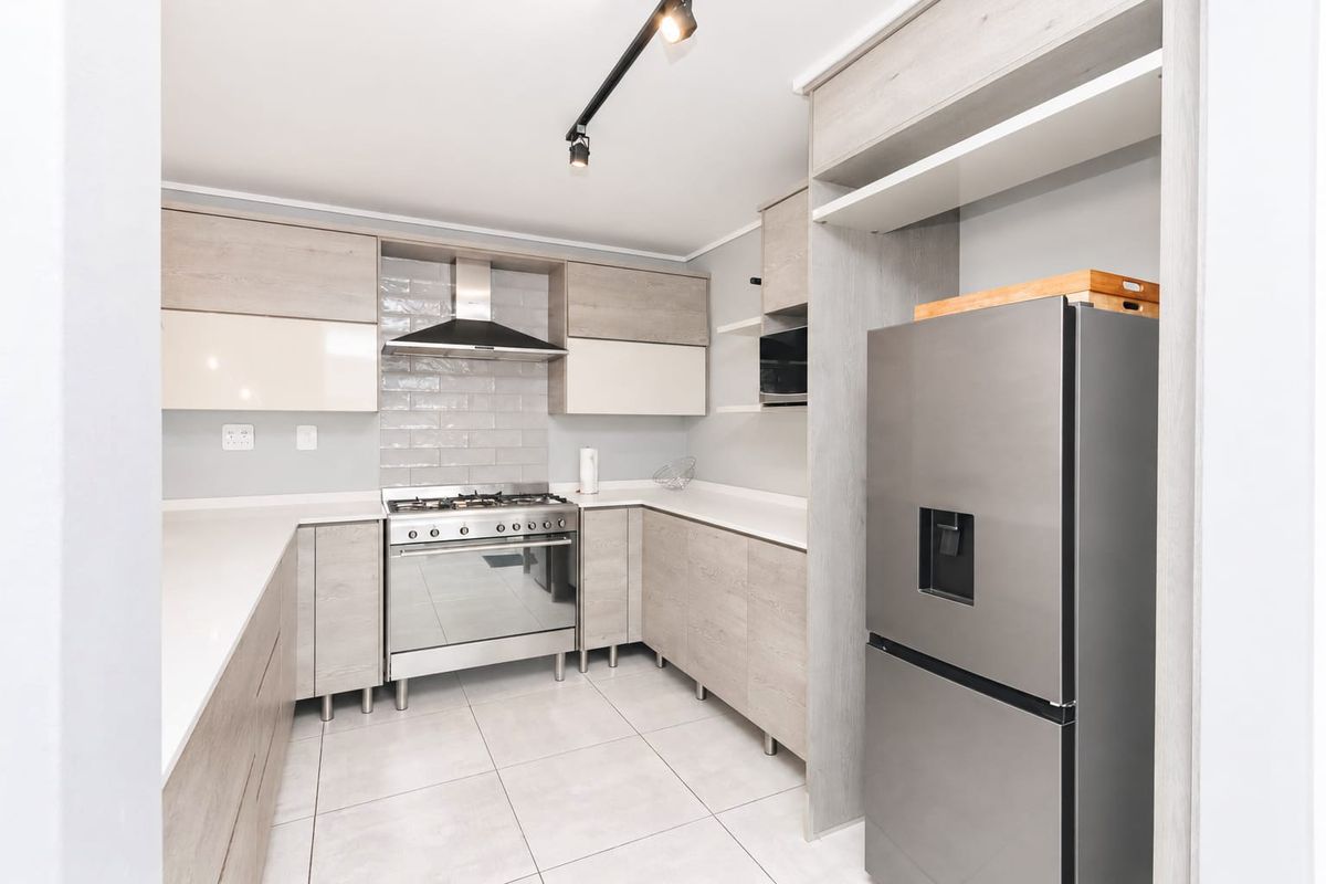 Modern kitchen featuring light wood-tone cabinetry, quartz countertops, a gas stove with extractor fan, and sleek tiled flooring.