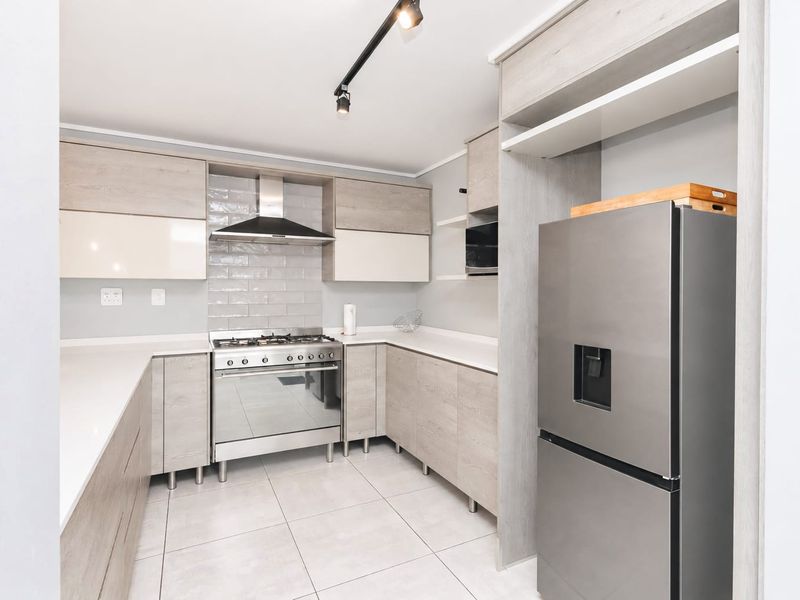 Modern kitchen featuring light wood-tone cabinetry, quartz countertops, a gas stove with extractor fan, and sleek tiled flooring.