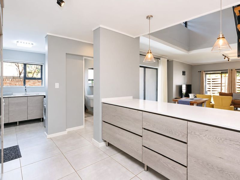 Modern open-plan living area featuring a sleek kitchen with stone countertops, contemporary cabinetry, tiled floors, and an integrated staircase leading to the upper level.