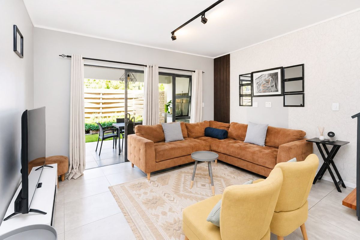A bright and modern living room featuring tiled floors, track lighting, and large sliding glass doors that open onto a private patio area.
