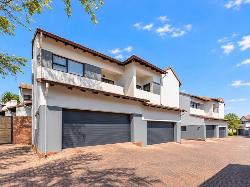 A modern townhouse exterior featuring a double garage, paved driveway, and upper-level balcony with a clean, well-maintained facade.