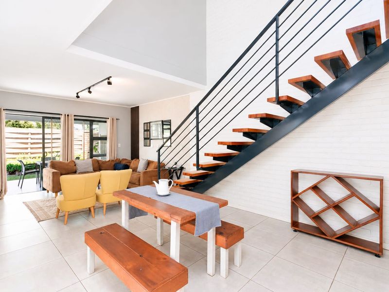 Spacious open-plan living area featuring a modern open-tread staircase, tiled flooring, and large sliding doors providing seamless access to the outdoor patio.