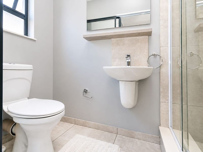 A clean, modern bathroom featuring a pedestal washbasin, a glass-enclosed shower, and neutral floor tiling with a minimalist aesthetic.