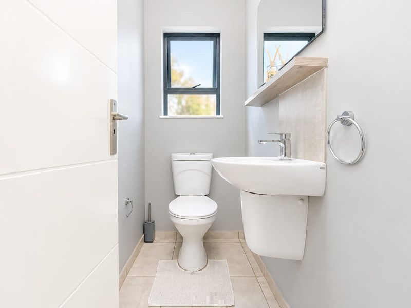 A clean and modern guest bathroom featuring a wall-mounted basin, toilet, tiled flooring, and a floating shelf with a mirror.