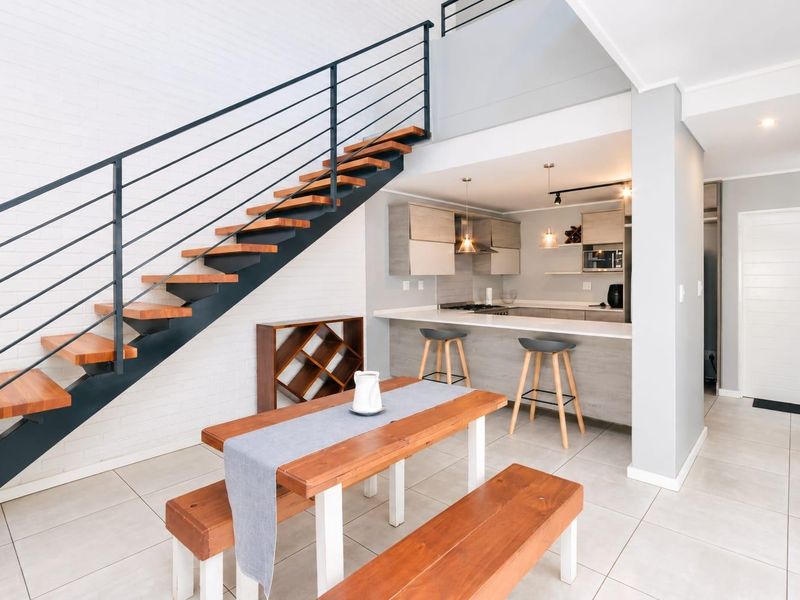 Modern open-plan living area featuring a contemporary staircase with timber treads, a sleek kitchen with stone countertops, and a breakfast bar.