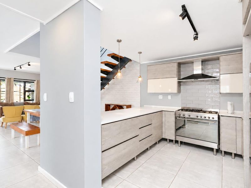Modern open-plan kitchen featuring light wood cabinetry, stone countertops, gas stove, and subway tile backsplash, seamlessly flowing into the adjacent living and dining area.