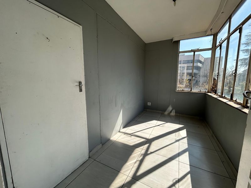 An empty, enclosed balcony or sunroom featuring tiled flooring and large windows, offering a bright space ready for renovation or repurposing.