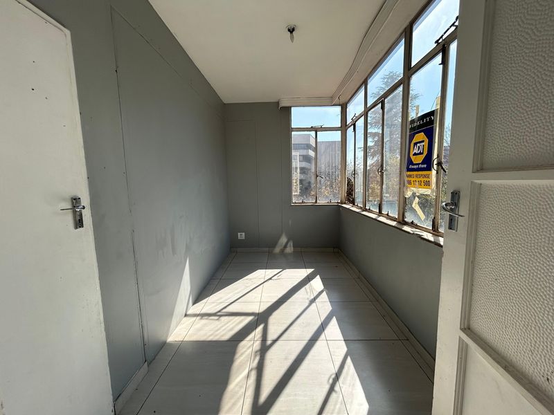 An enclosed balcony or sunroom featuring tiled flooring and large metal-framed windows, offering a bright, versatile space ready for renovation or staging.